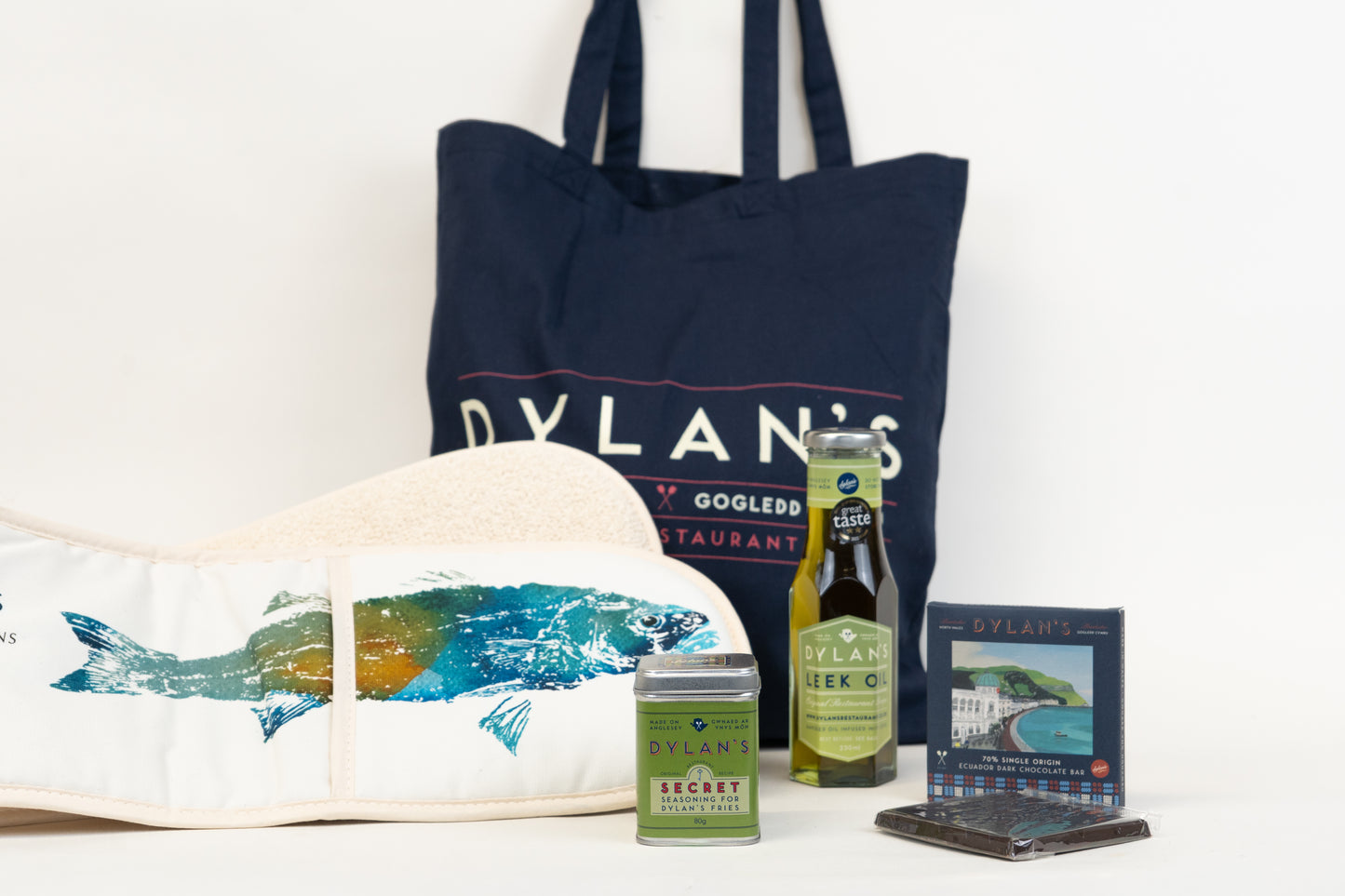 Navy tote bag with 'Dylan's' branding, a white tote bag with fish design, and various items on a white background.