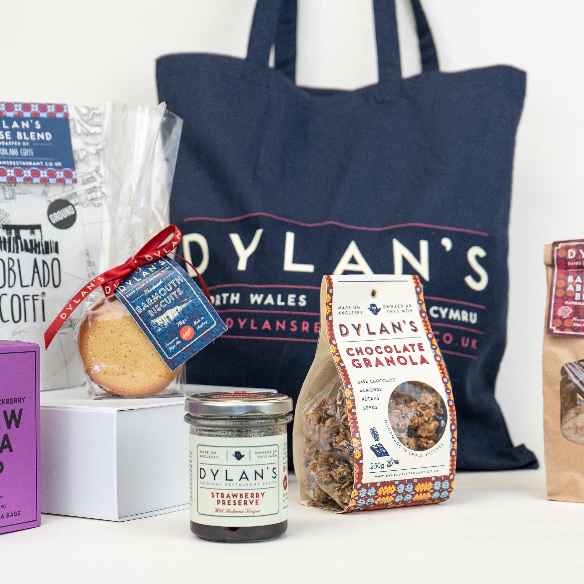 Assorted Dylan's products including coffee, tea, and cookies with a blue tote bag in the background.