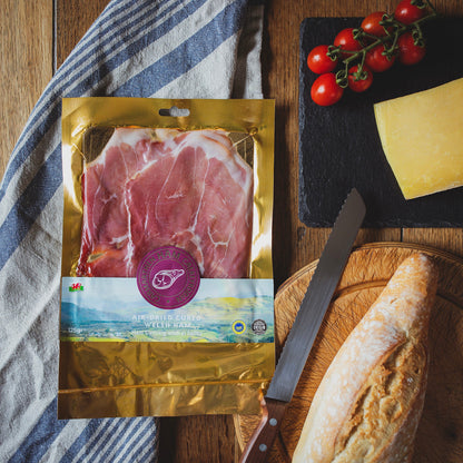 Packaged air-dried cured Welsh ham with gold packaging on a table with bread and tomatoes