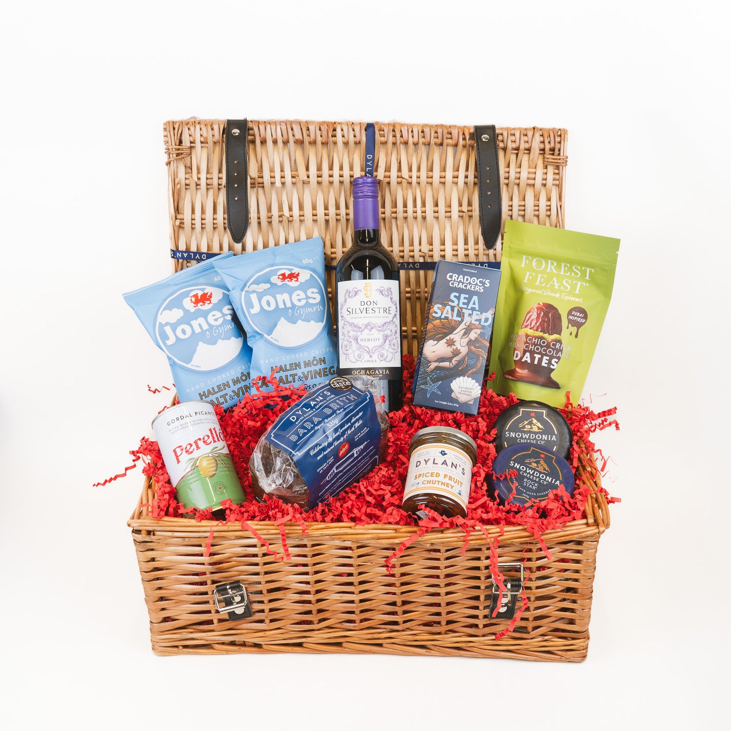 Wicker gift basket with assorted products including wine, snacks, and treats on a white background