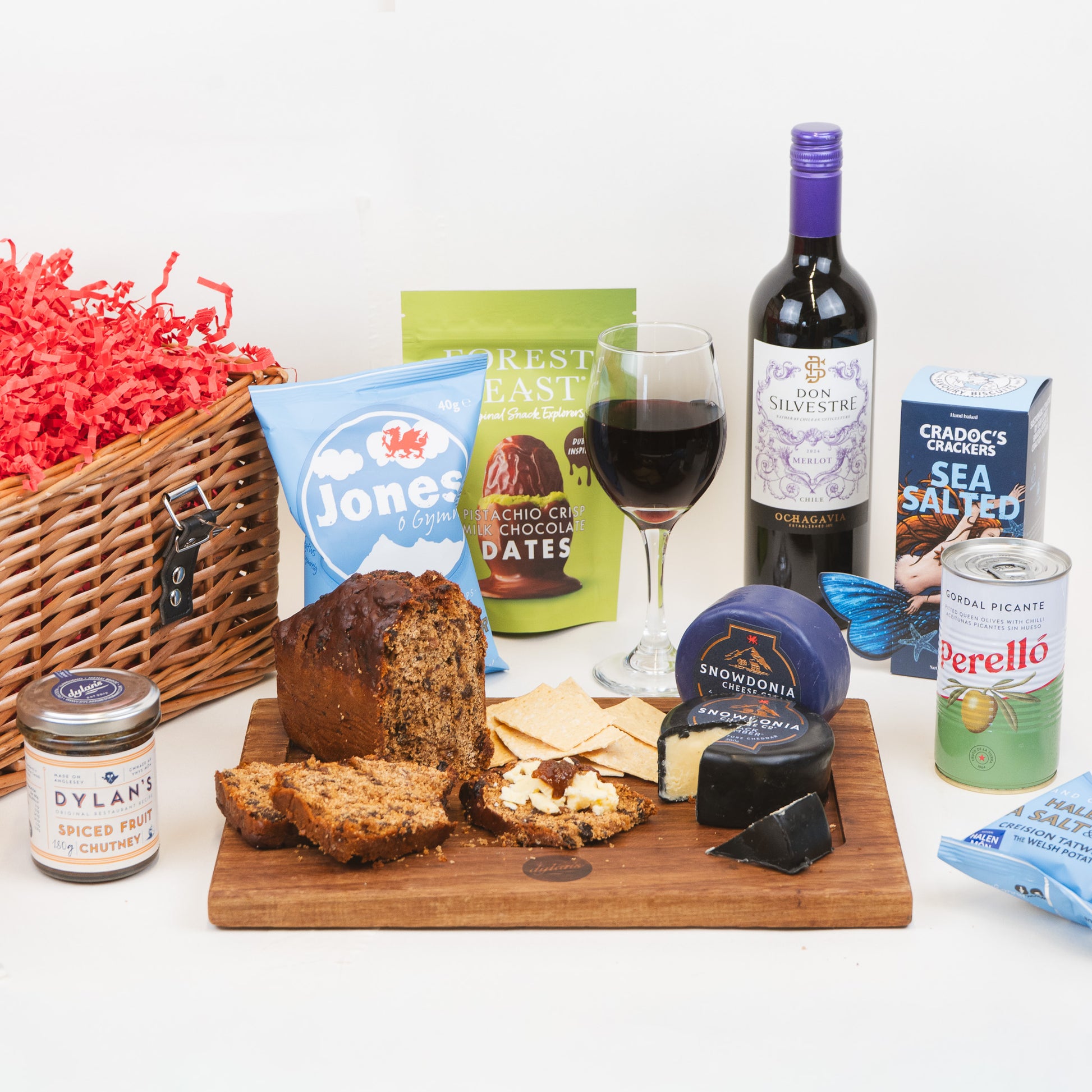 Gourmet gift basket with bread, cheese, wine, and other snacks on a white background